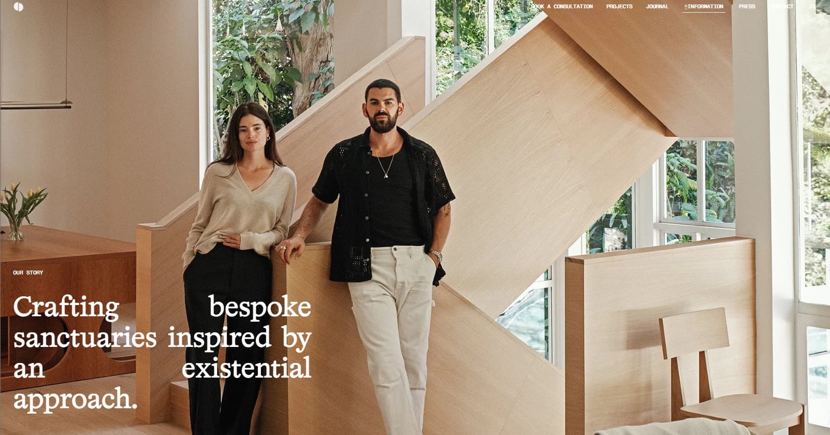 Ome Dezin website image showing two people beside a sculptural wooden staircase in a bright interior.